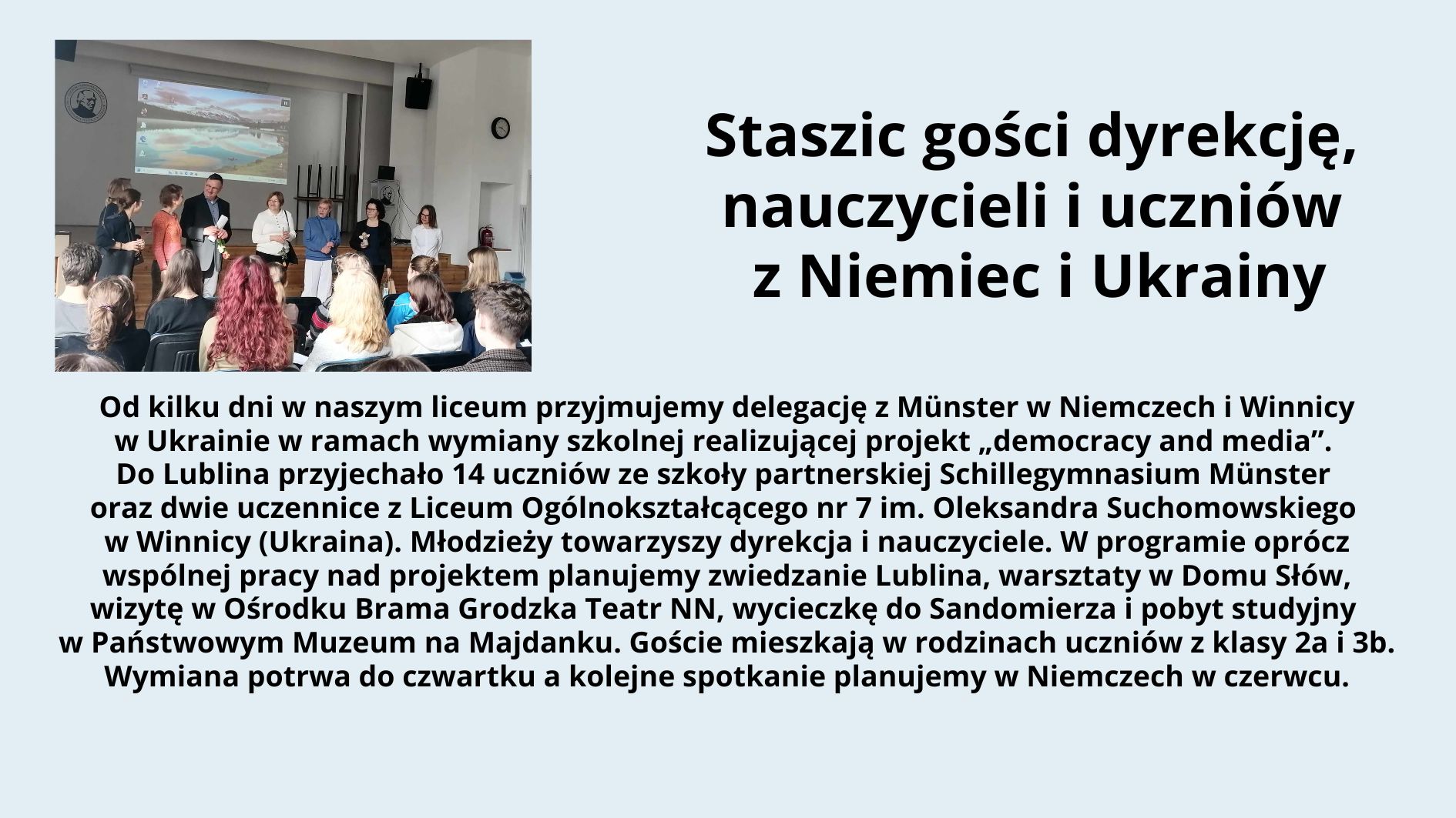 Grafika składa się z dwóch części: zdjęcia po lewej stronie oraz tekstu po prawej stronie na jasnoniebieskim tle. Zdjęcie: Przedstawia scenę w sali szkolnej z drewnianą podłogą i białymi ścianami. Na ścianie w tle widoczny jest ekran z projektorem, na którym wyświetlono obraz przedstawiający krajobraz z wodą i górami. Na scenie stoi siedem osób – pięć dorosłych i dwie młodsze osoby, prawdopodobnie uczniowie. Dorośli są elegancko ubrani – mężczyzna w garniturze, kobiety w swetrach lub marynarkach. Wśród nich jedna osoba trzyma mikrofon, a reszta uśmiecha się i patrzy na publiczność. Publiczność składa się z uczniów siedzących na krzesłach; niektórzy mają widoczne kolorowe ubrania, w tym dziewczyna z długimi rudymi włosami w czerwonej bluzie. Tekst: Po prawej stronie znajduje się blok tekstu w języku polskim. Nagłówek w dużej czarnej czcionce głosi: „Staszic gości dyrekcję, nauczycieli i uczniów z Niemiec i Ukrainy” Poniżej znajduje się akapit tekstu w mniejszej czcionce: Od kilku dni w naszym liceum przyjmujemy delegację z Münster w Niemczech i Winnicy w Ukrainie w ramach wymiany szkolnej realizującej projekt „democracy and media”. Do Lublina przyjechało 14 uczniów ze szkoły partnerskiej Schillegymnasium Münster oraz dwie uczennice z Liceum Ogólnokształcącego nr 7 im. Oleksandra Suchomowskiego w Winnicy (Ukraina). Młodzieży towarzyszy dyrekcja i nauczyciele. W programie oprócz wspólnej pracy nad projektem planujemy zwiedzanie Lublina, warsztaty w Domu Słów, wizytę w Ośrodku Brama Grodzka Teatr NN, wycieczkę do Sandomierza i pobyt studyjny w Państwowym Muzeum na Majdanku. Goście mieszkają w rodzinach uczniów z klasy 2a i 3b. Wymiana potrwa do czwartku a kolejne spotkanie planujemy w Niemczech w czerwcu. Cała grafika jest estetycznie uporządkowana, z dobrze widocznym tekstem na kontrastowym tle, co poprawia czytelność.