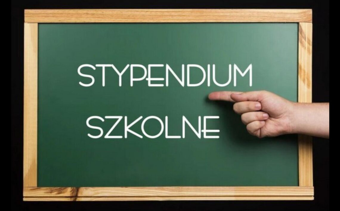 Obraz przedstawia ciemnozieloną szkolną tablicę w drewnianej ramie, umieszczoną na czarnym tle. W centrum tablicy znajduje się biały, prosty, nowoczesny napis pisany wielkimi literami: „STYPENDIUM SZKOLNE”. Dodatkowe elementy: Po prawej stronie obrazu, na wysokości napisu, widoczna jest ludzka dłoń z jasną karnacją, ułożona poziomo z wyprostowanym palcem wskazującym, który wskazuje bezpośrednio na napis „STYPENDIUM”. Tło poza tablicą jest całkowicie czarne, co podkreśla kontrast i skupia uwagę na napisie. Symbolika i kontekst: Obraz w wyraźny sposób wskazuje na temat pomocy finansowej dla uczniów – stypendium szkolne. Użycie szkolnej tablicy i gestu wskazującego ma za zadanie zwrócić uwagę odbiorcy na ważność tematu.
