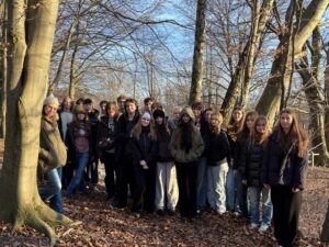 Grupowe zdjęcie młodzieży stojącej w lesie między drzewami, ubranej w zimowe kurtki, wykonane podczas wycieczki.
