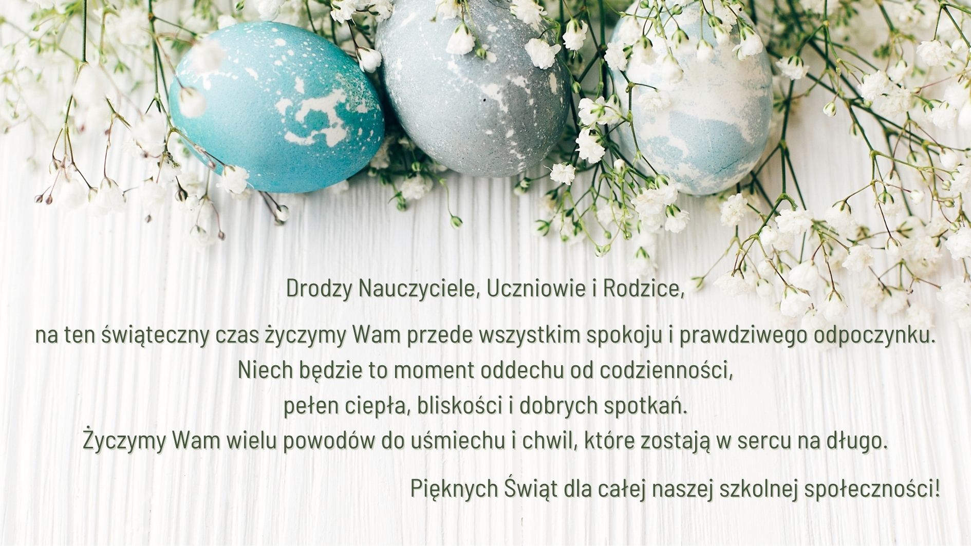 Grafika przedstawia trzy pastelowe jajka wielkanocne (niebieskie i szare) ozdobione białymi plamkami, ułożone wśród drobnych, białych kwiatów na jasnym, drewnianym tle. Na środku znajduje się tekst z życzeniami świątecznymi skierowany do nauczycieli, uczniów i rodziców, dotyczący spokoju, odpoczynku oraz radosnych chwil.