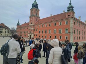 Uczniowie z nauczycielami stoją na placu Zamkowym w Warszawie obok Zamku Królewskiego.