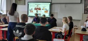 Zbliżenie na symulację rozprawy: uczniowie siedzą przy stołach, „sędziowie” z przodu, a jedna osoba stoi i składa wypowiedź.