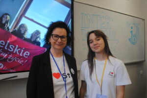 Nauczycielka i uczennica stoją obok siebie przy tablicy z napisem „International Baccalaureate”.