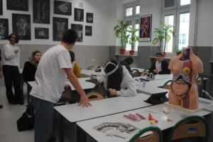 Uczniowie w pracowni biologicznej korzystają z gogli VR; na stole model ludzkiego tułowia i materiały promocyjne.