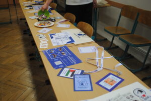 Stół z materiałami promocyjnymi: identyfikatory, ulotki, smycze i miska z cukierkami.