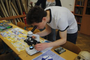 Uczeń pochyla się nad mikroskopem i obserwuje preparat na stoliku laboratoryjnym.