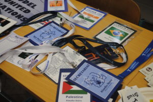 Zbliżenie na identyfikatory i smycze z wydarzenia (m.in. „SECRETARIAT”, „STAŚMUN 2025”, nazwy krajów i organizacji).