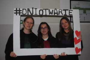 Trzy uczennice pozują w dużej ramce z napisem „#DNIOTWARTE” i czerwonymi sercami. 