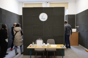 Pomieszczenie wyciszone pianką akustyczną z logo „Stasie Radio”. Przy stole stoją krzesła i materiały, a kilka osób ogląda wnętrze.