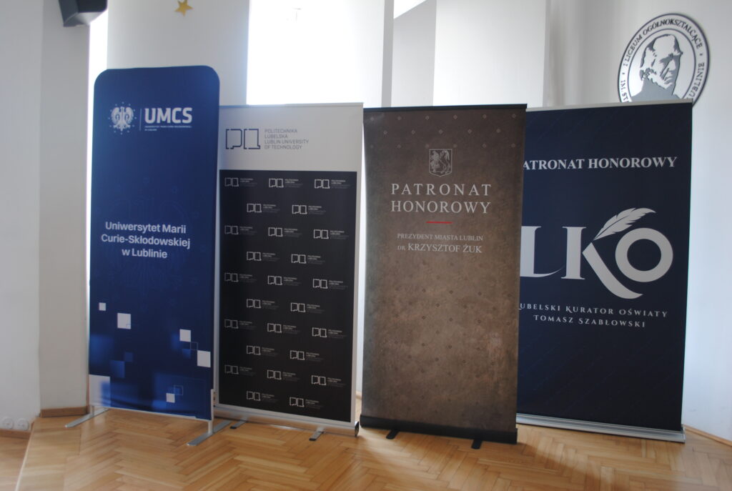 Roll-upy partnerów i patronów wydarzenia ustawione w sali konferencyjnej.