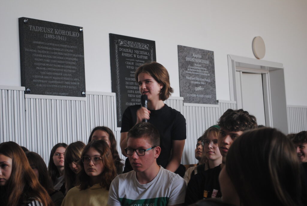 Uczeń z mikrofonem zadaje pytanie podczas dyskusji wśród uczestników konferencji.