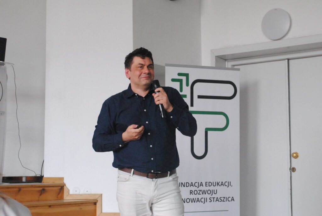 Prelegent występuje na scenie obok roll-upu Fundacji Edukacji, Rozwoju i Innowacji Staszica.