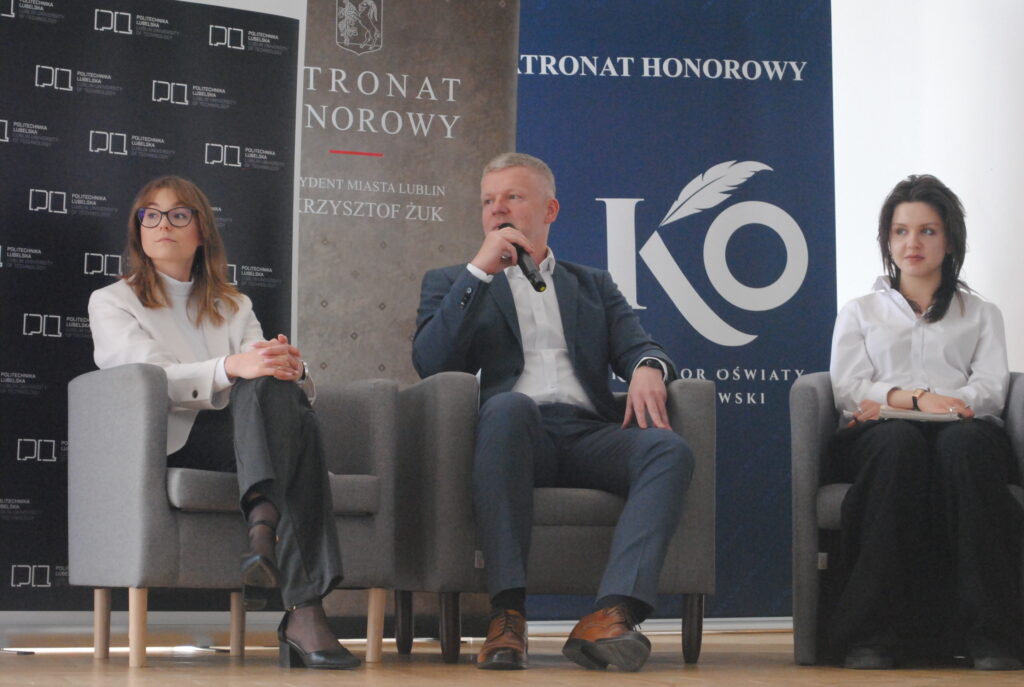 Panel dyskusyjny z udziałem trzech osób siedzących w fotelach na scenie.