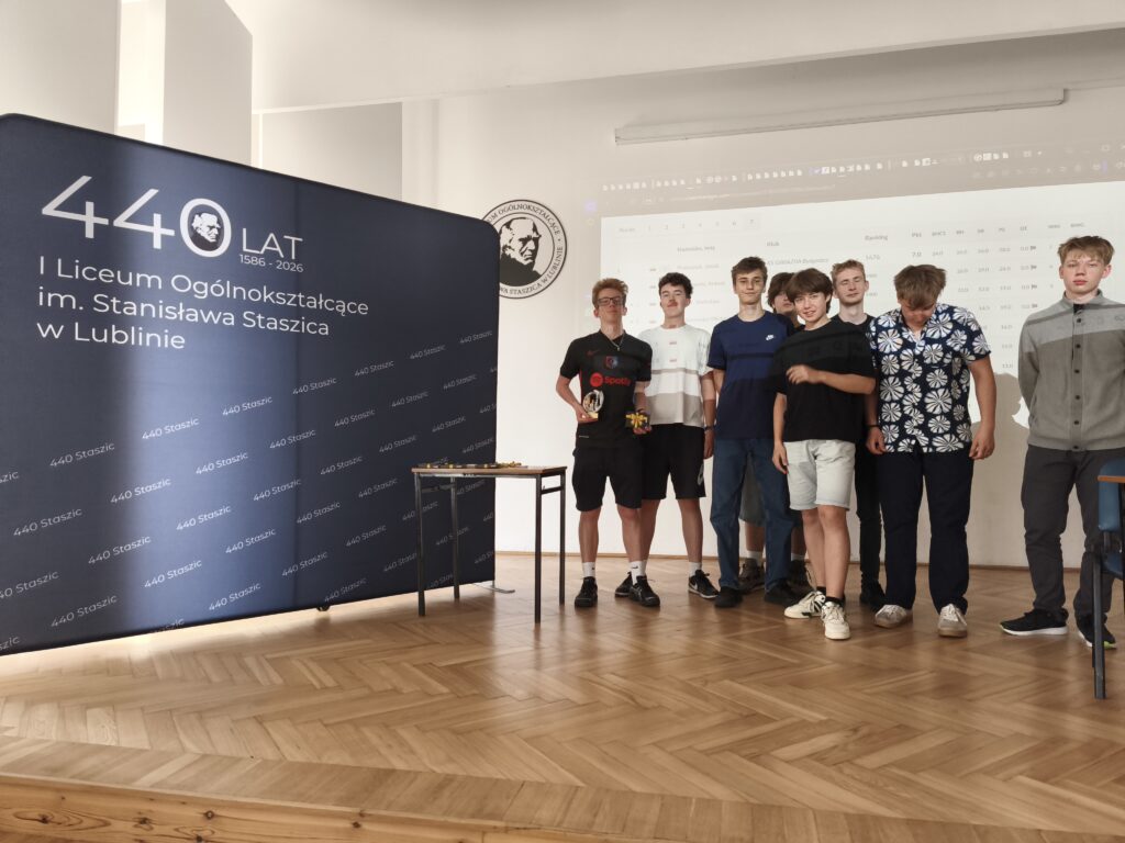 Kilku uczniów stoi obok siebie na tle granatowej ścianki z napisem „440 Staszic”. Pozują do wspólnego zdjęcia po zakończeniu wydarzenia, uśmiechając się do aparatu. Fotografia dokumentuje uczestników turnieju.