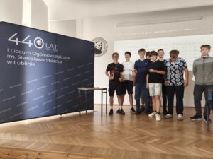 Kilku uczniów stoi obok siebie na tle granatowej ścianki z napisem „440 Staszic”. Pozują do wspólnego zdjęcia po zakończeniu wydarzenia, uśmiechając się do aparatu. Fotografia dokumentuje uczestników turnieju.