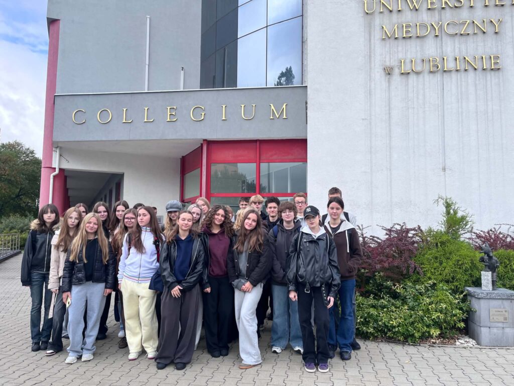 Grupowe zdjęcie uczniów przed budynkiem Collegium Uniwersytetu Medycznego w Lublinie. Kilkudziesięciu młodych ludzi stoi przed wejściem do budynku. Nad nimi widoczny jest napis „COLLEGIUM”, a na elewacji fragment nazwy „Uniwersytet Medyczny w Lublinie”.