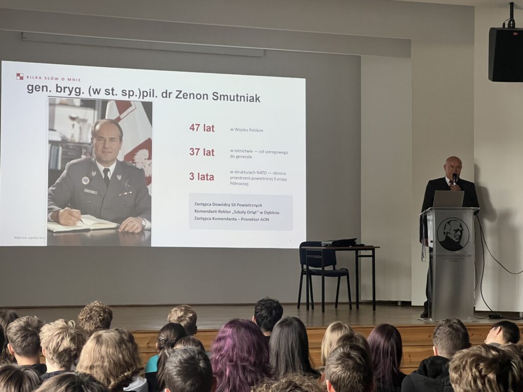 Prelegent omawia zagadnienia bezpieczeństwa Polski, prezentując slajd z tekstem i grafiką.